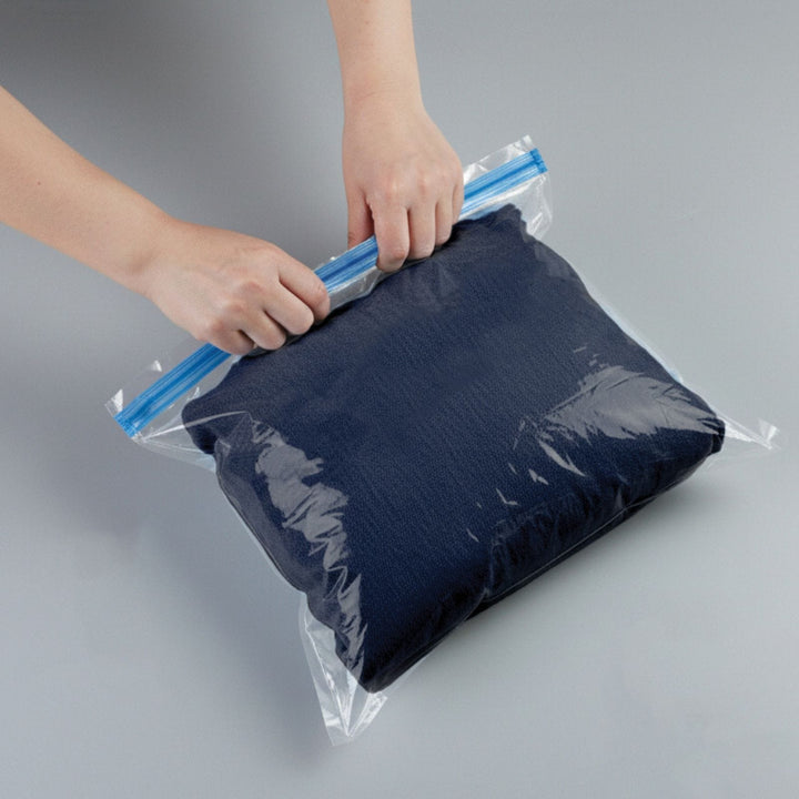 persons hands about to roll down the compression bag with pair of jeans inside