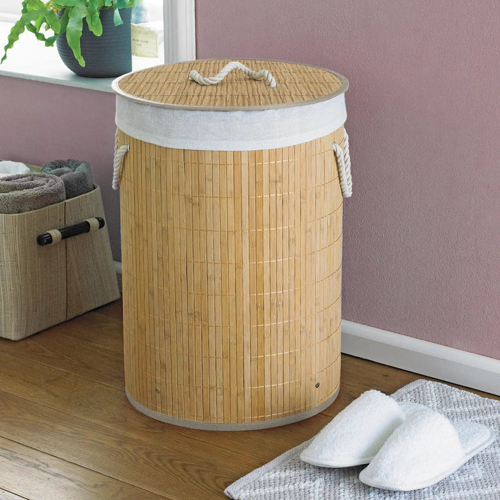 Natural colour bamboo and rattan laundry basket with white rope handles in a room with slippers and towels