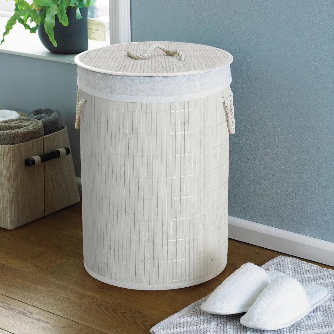 White bamboo and rattan laundry basket with white rope handles in a room with slippers and towels