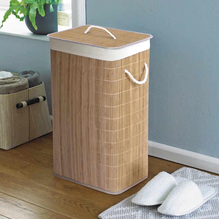 Natural bamboo and rattan laundry hamper with white rope handles in a room with slippers and towels