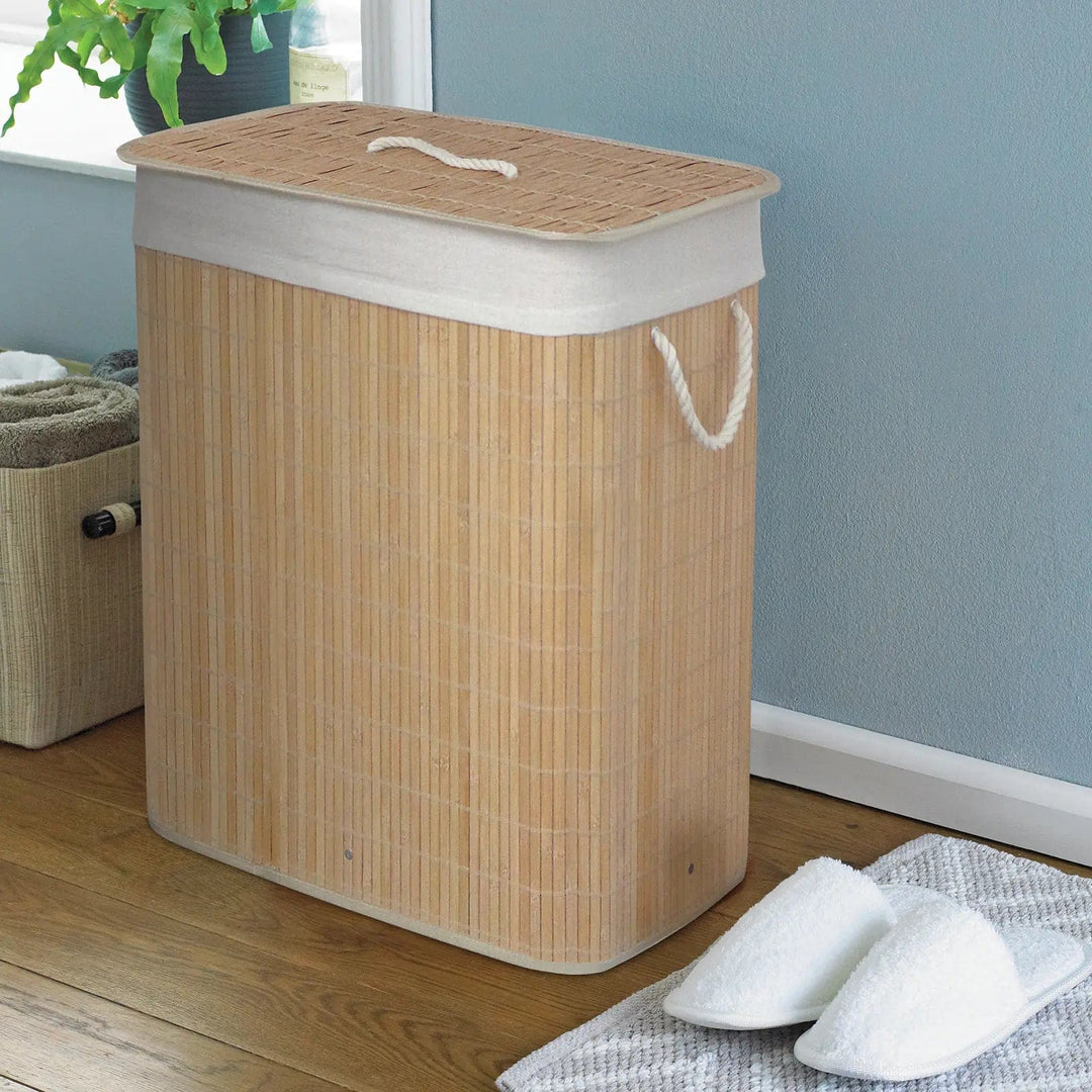 Beige bamboo laundry basket with white rope handles in a room with slippers and pot plant