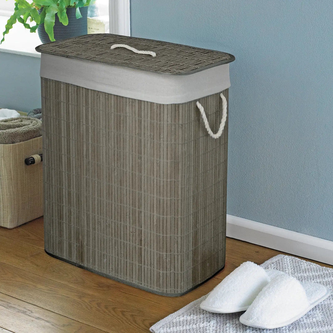 Grey bamboo laundry basket with white rope handles in a room with slippers and pot plant