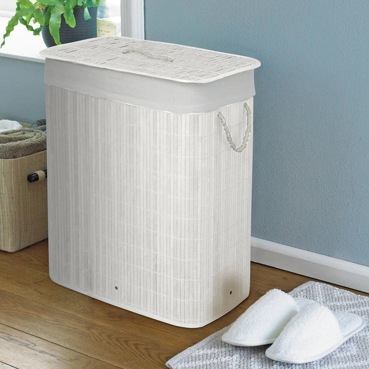 White bamboo laundry basket with white rope handles in a room with slippers and pot plant