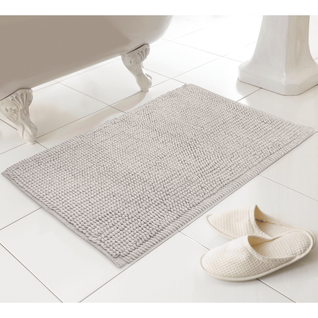 neutral stone colour bobble texture bath mat in bathroom floor with slippers to the side
