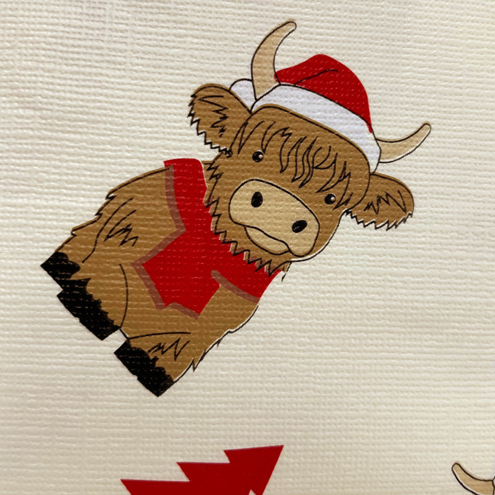Close up detail of a Highland cow with a red and white Santa hat and red jumper on a cream background