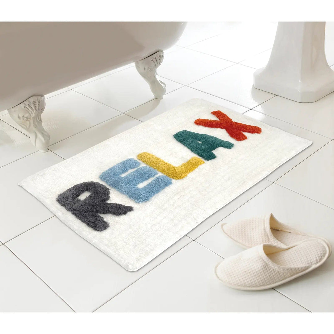 Words bath mat with relax letters in bright colours on a tiled floor next to a bath and slippers