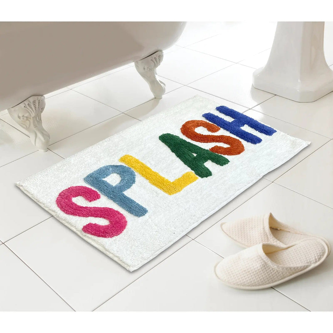 Words bath mat with Splash letters in bright colours on a tiled floor next to a bath and slippers