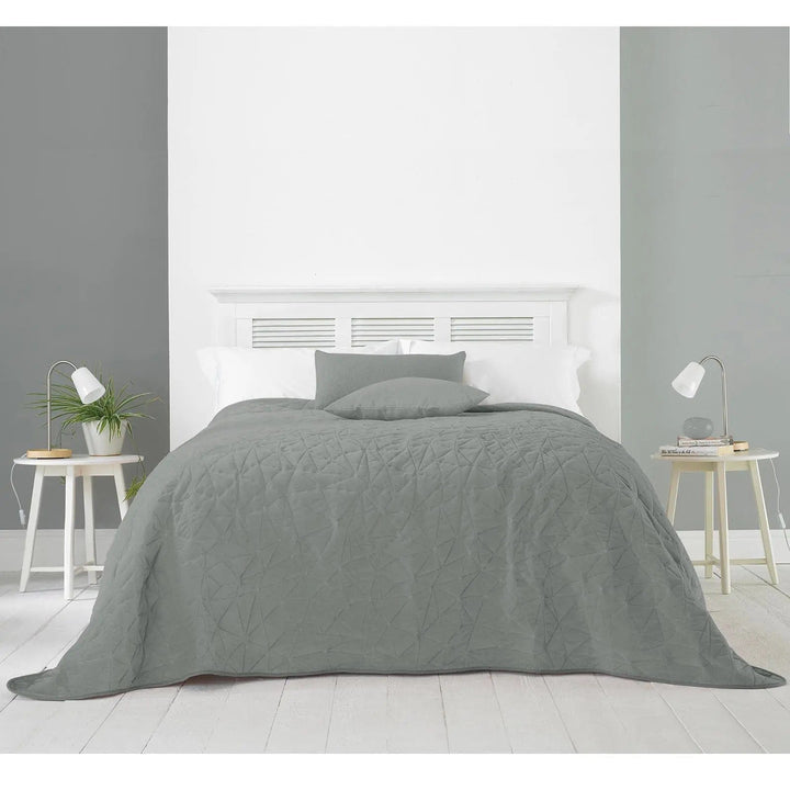 Grey bedspread with geometric pattern darpaed over a bed with side tables and lamps