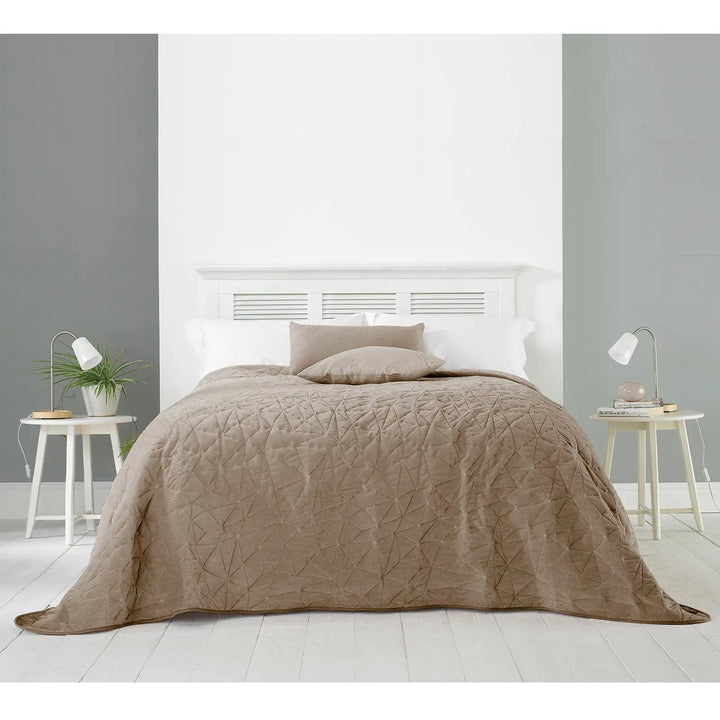 Taupe beige bedspread with geometric pattern darpaed over a bed with side tables and lamps