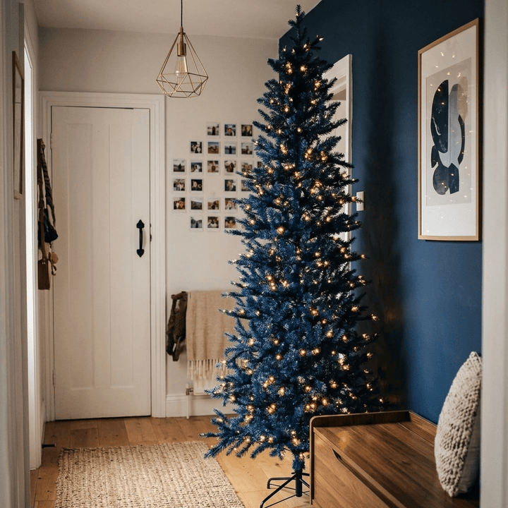 Decorative blue Christmas tree in a room with a wooden bench and framed picture on a blue wall.