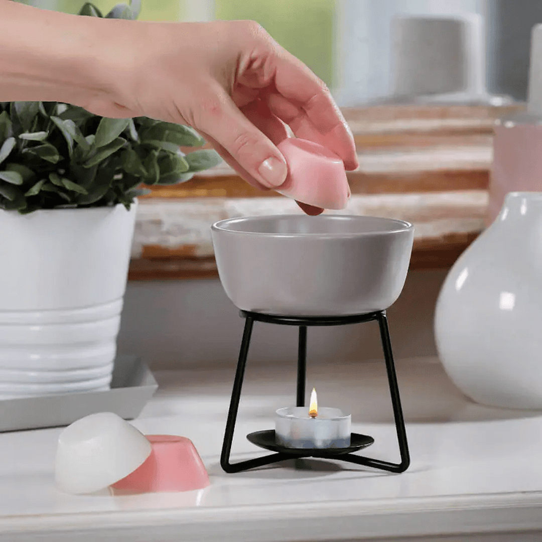 unidentified persons hand placing wax melt into grey wax melt burner on table