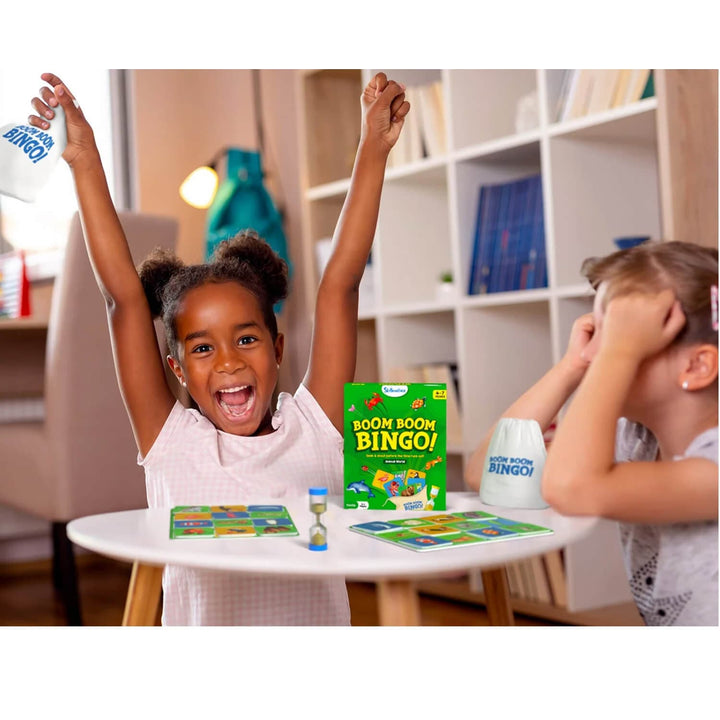 Two children playing with Boom Boom Bingo game in a room with shelves and books.