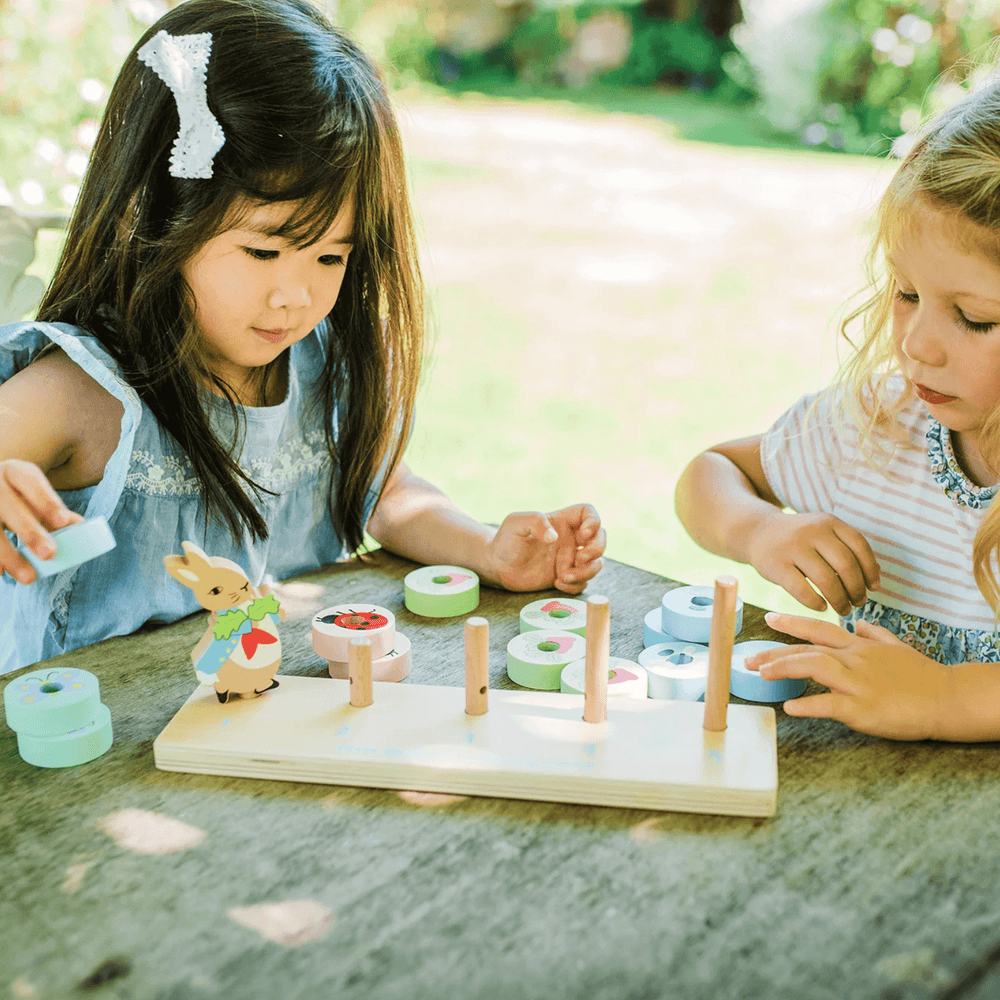 two little girls play with peter rabbit counting game in garden on wooden picnic bench
