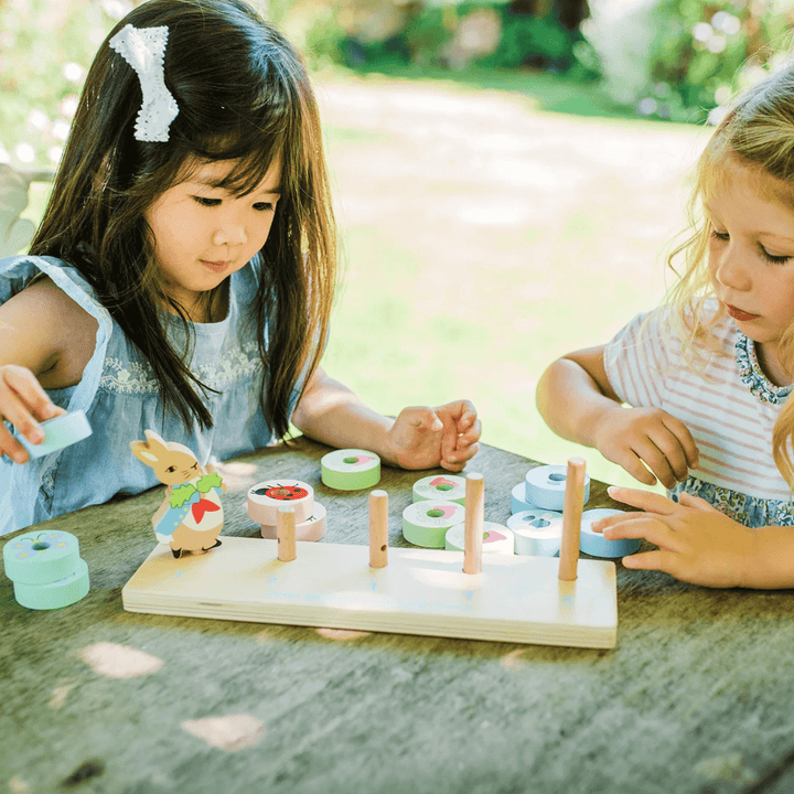 two little girls play with peter rabbit counting game in garden on wooden picnic bench