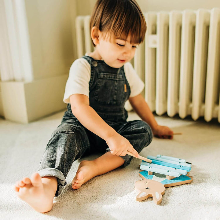 Toddler playing on the floor with a Peter Rabbit xylophone with 5 bars and 2 drumsticks