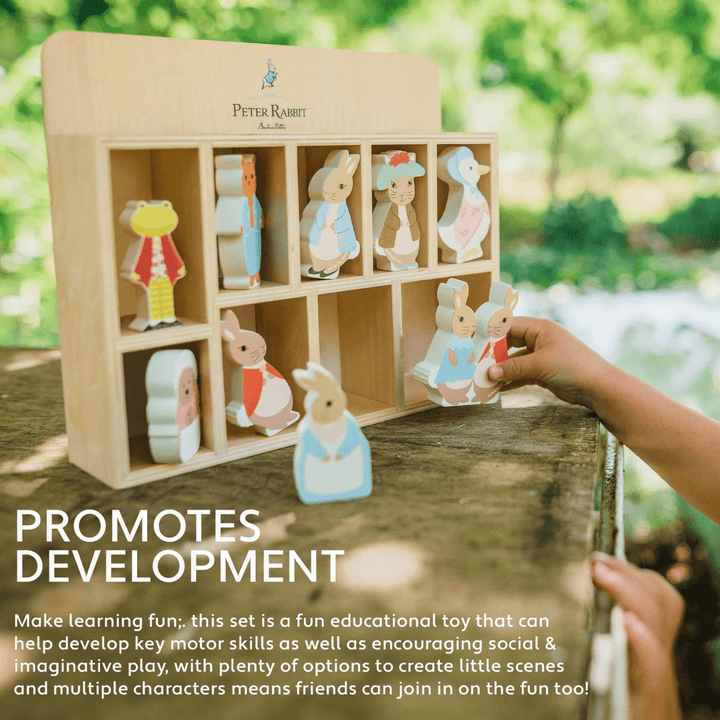 little girls hands holds peter rabit characters in beside display shelf on a wooden outdoor table with trees in background