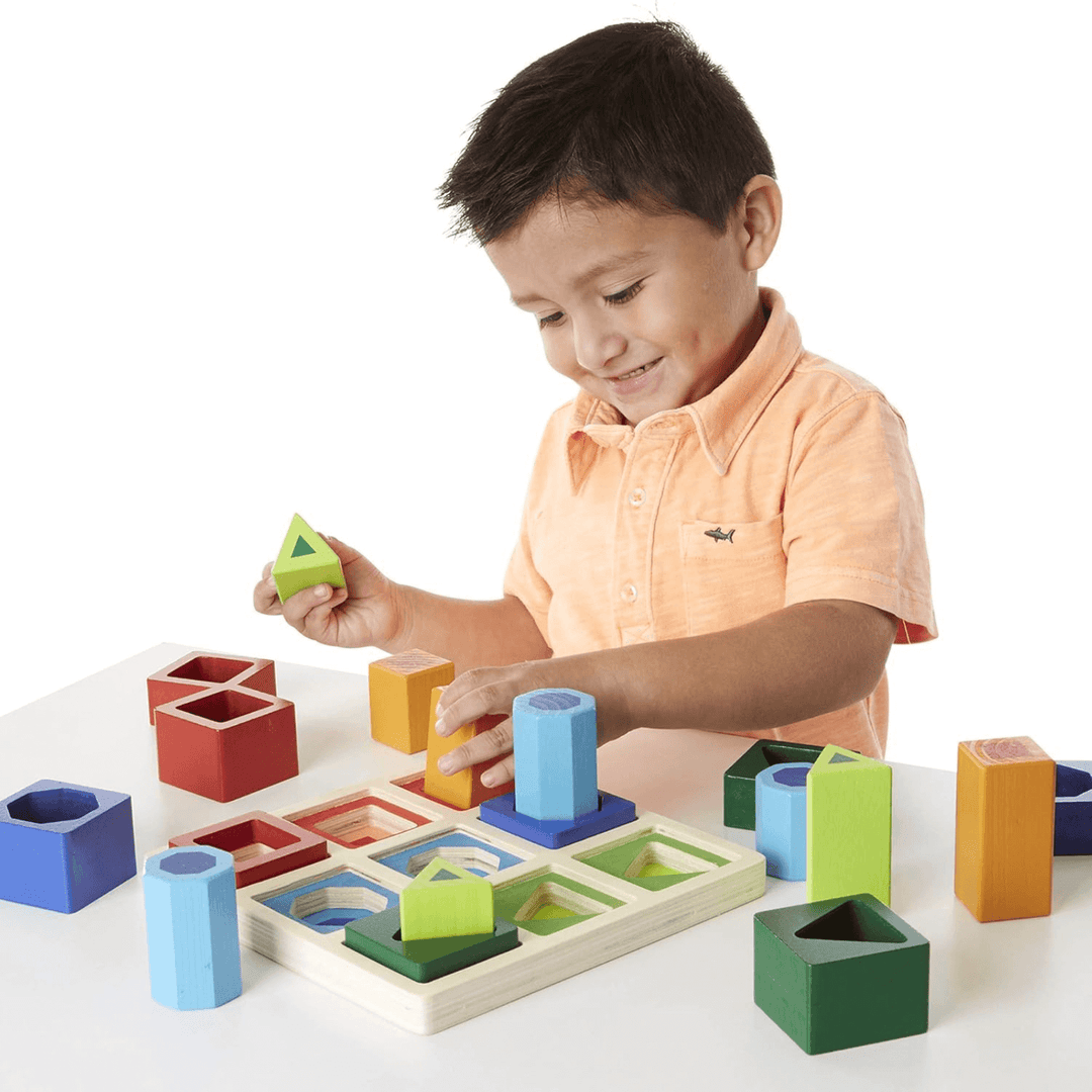 little boy smiles as he inserts cube shape into wooden shape sorter frame