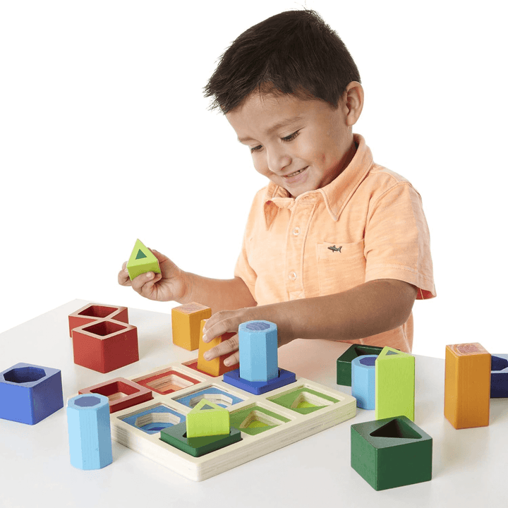 little boy smiles as he inserts cube shape into wooden shape sorter frame