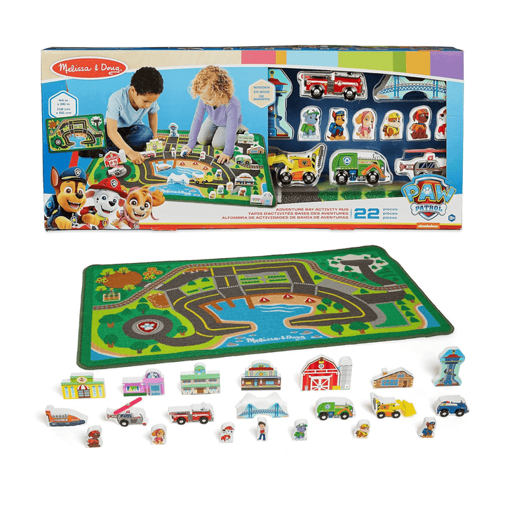 PAW Patrol adventure bay activity rug in cardboard packaging with includes wooden figures, buildings and vehicles laid out beside printed rug on white background