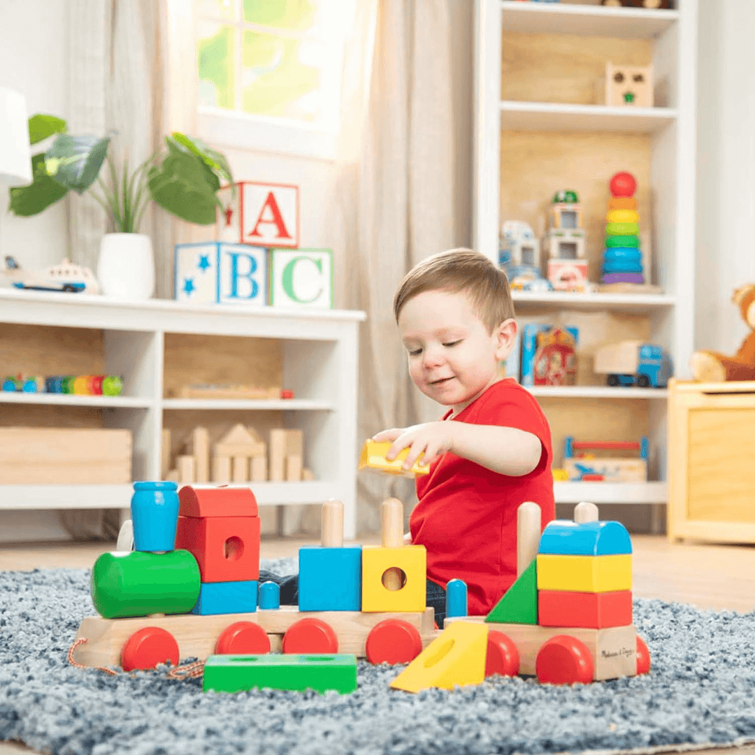 little boy stacks yellow block onto train as he plays in his bedoom