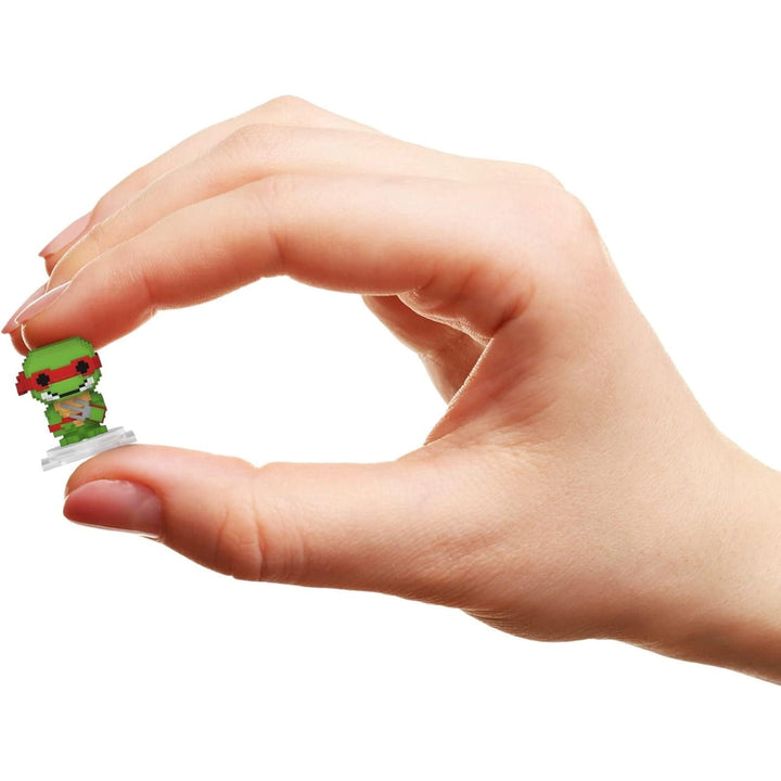 Hand holding a small green 8-bit figurine against a white background