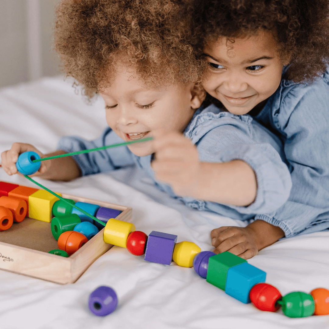 two young girls smile as they play with the wooden lacing bead set