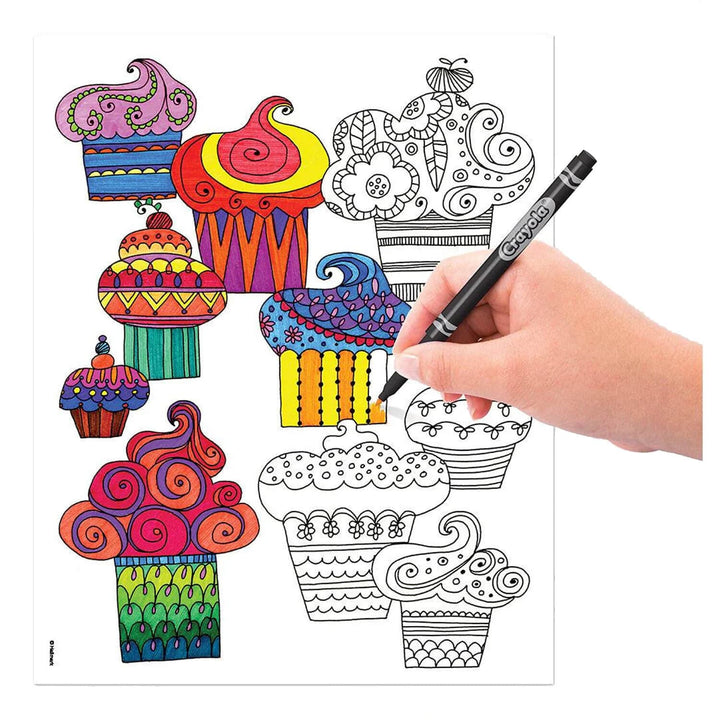 A hand holding a Crayola marker is colouring a black-and-white cupcake coloring page with several colourful, fully coloured cupcake designs shown around it on a white background.