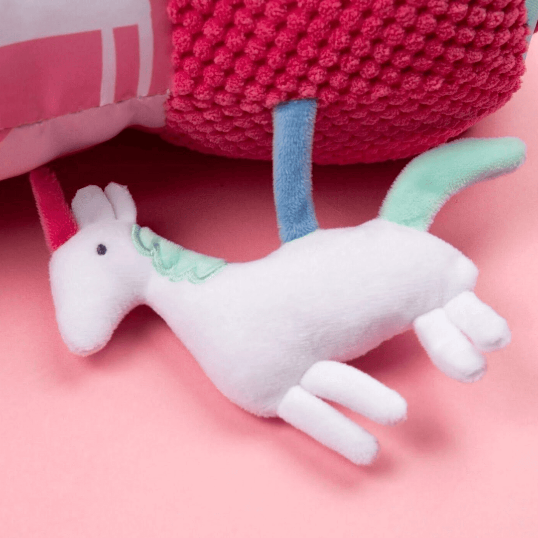 white unicorn squeaker toy on pink coloured tummy time roller.