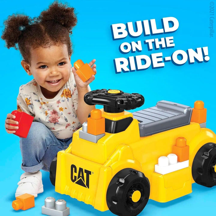 Girl with building blocks to add to a yellow Caterpillar ride on truck