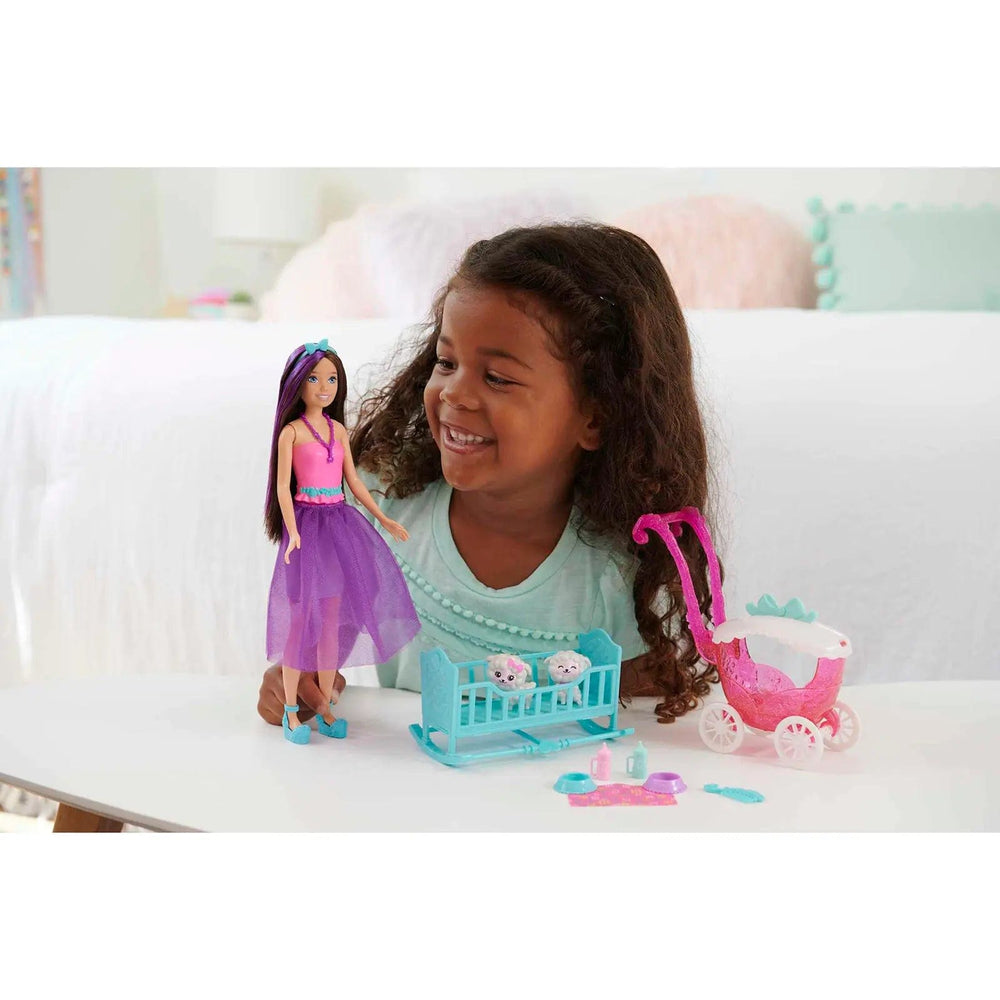 Child playing with a Barbie doll dressed in pink and purple with cot and pushchair accessories