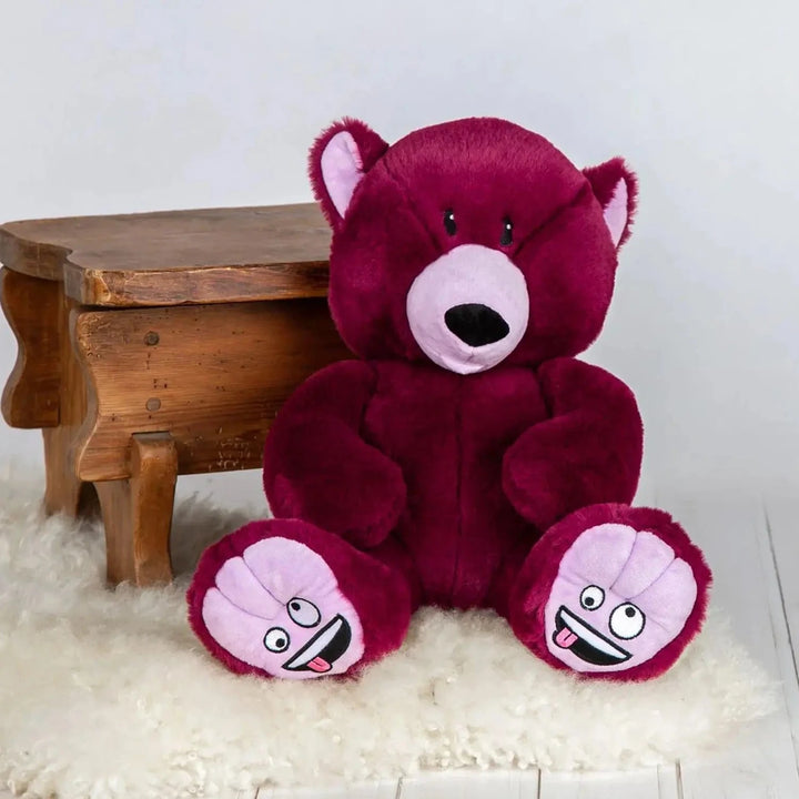 Purple Silly Mood Bear sitting on a rug beside a wooden stool