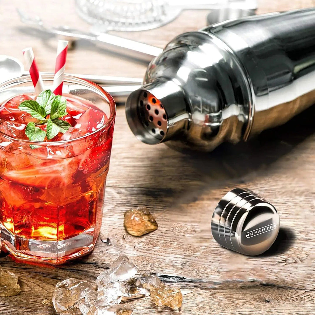 Nuvantee polished stainless steel cocktail shaker lying next to a red cocktail with mint leaves and candy stripe straws