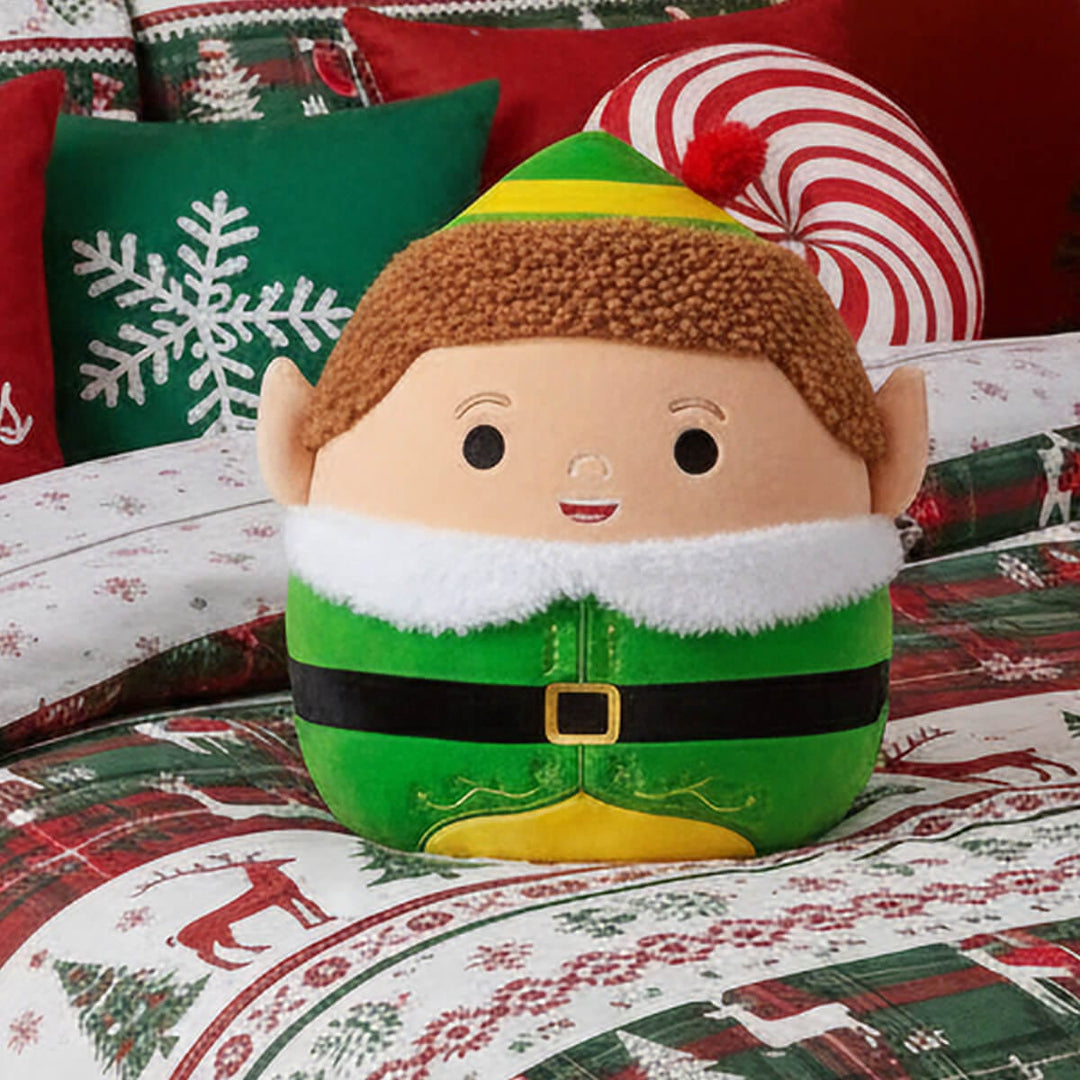 buddy the elf squishmallow figure on a bed with Christmas theme duvet cover and pillows