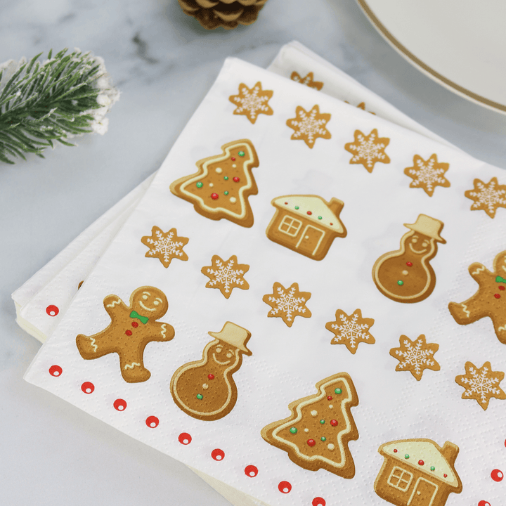 gingerbread table napkin pile sitting on christmas table beside plate and pine cone decorations