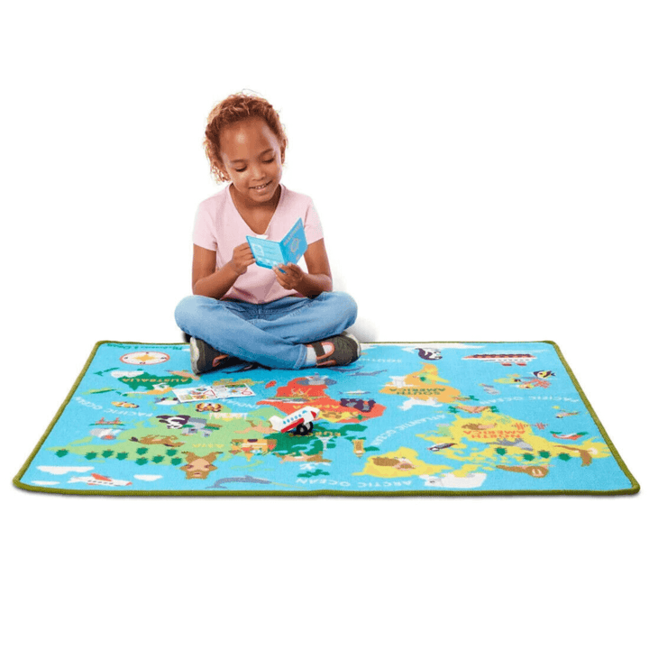 little girl sits on play mat and looks at her pretend play passport smiling