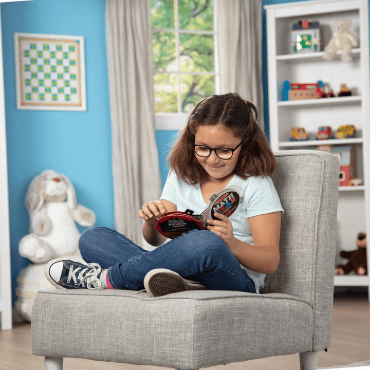 little girl sits on chair in her bedroom smiling as she uses the math gear booklet to learn division maths
