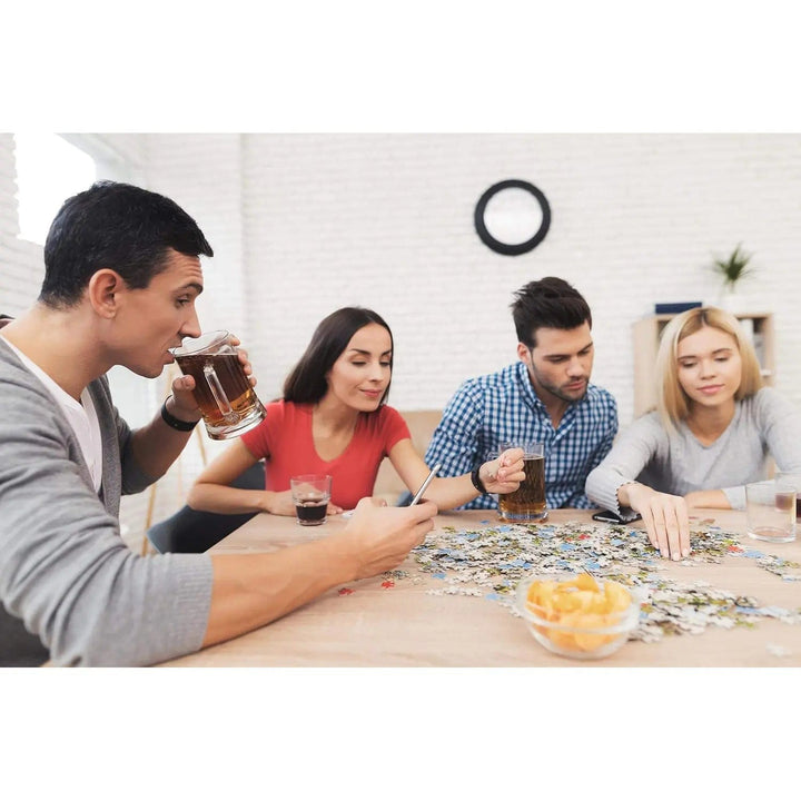 4 adults with drinks and snacks completing a jigsaw puzzle on a table