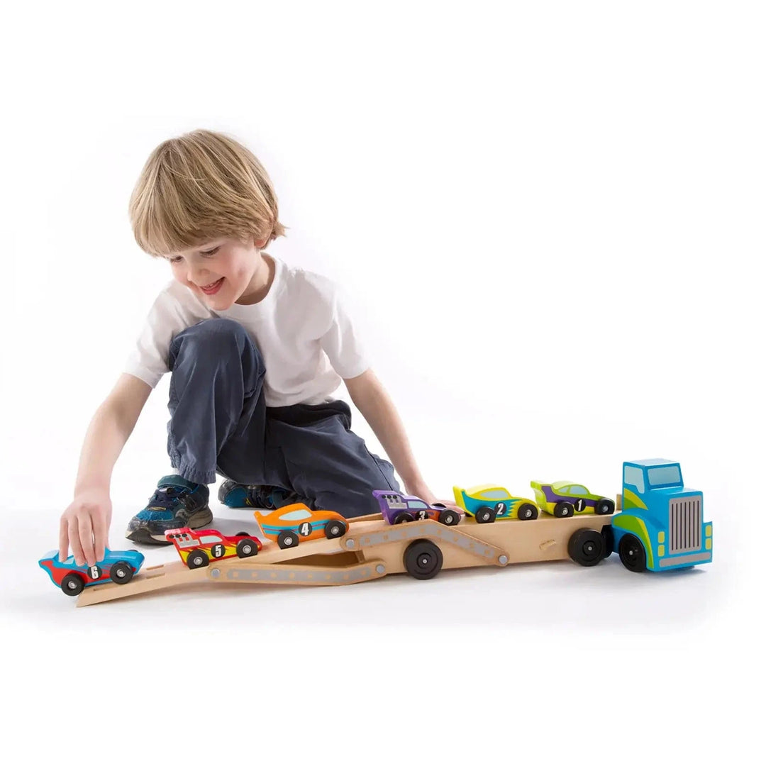 Child loading race cars onto the top deck of a large wooden transporter truck