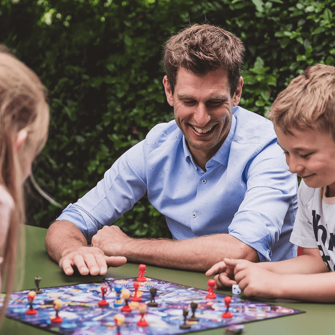 a dad and his kids playing the board game on a table in the garden, smiling