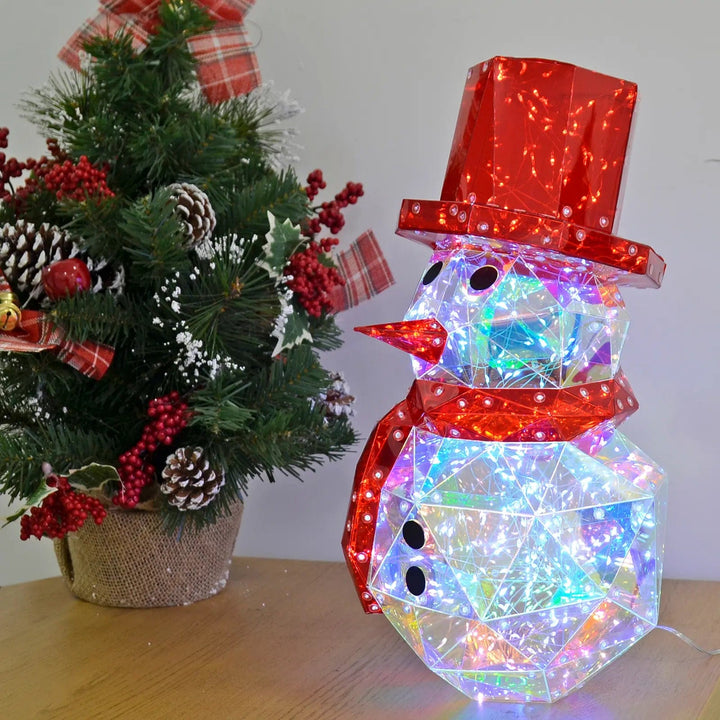 Light up Starlightz Christmas Snowman lamp with red hat and scarf on a table with decorated Christmas tree