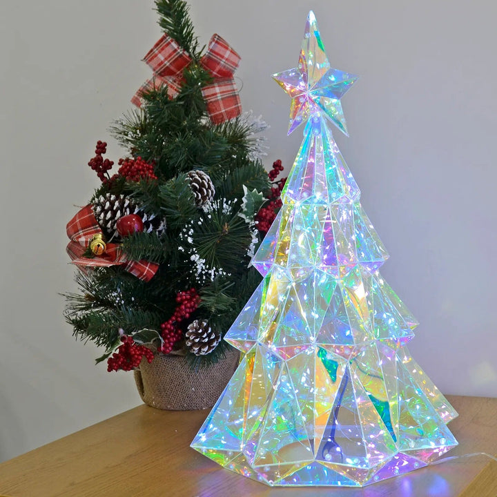 Starlightz LED Christmas tree light on a table next to a mini decorated Christmas tree