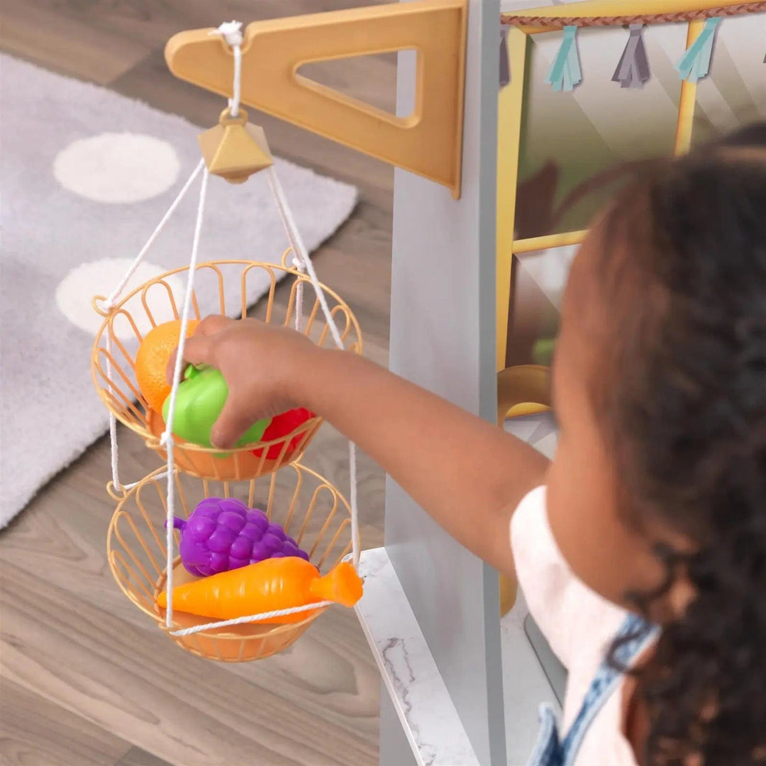 Girl taking pretend fruit out of a hanging basket in a play kitchen