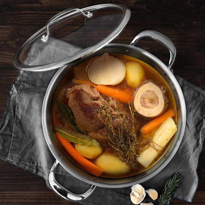 Overhead view of a large stock pot filled with meat, vegetables and herbs, with glass lid