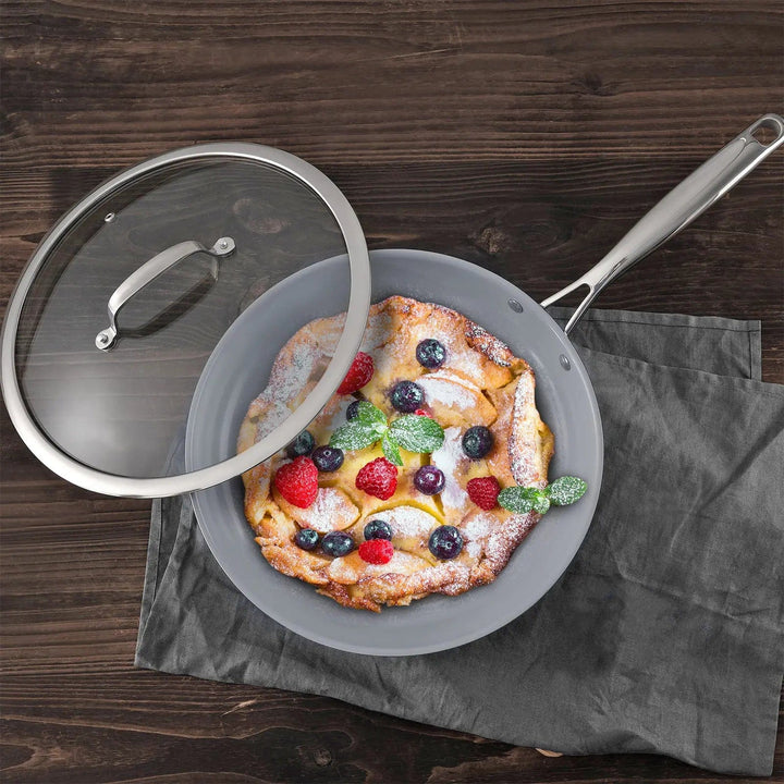 Overhead view of a frying pan with lid set aside to show a baked apple dessert with berries