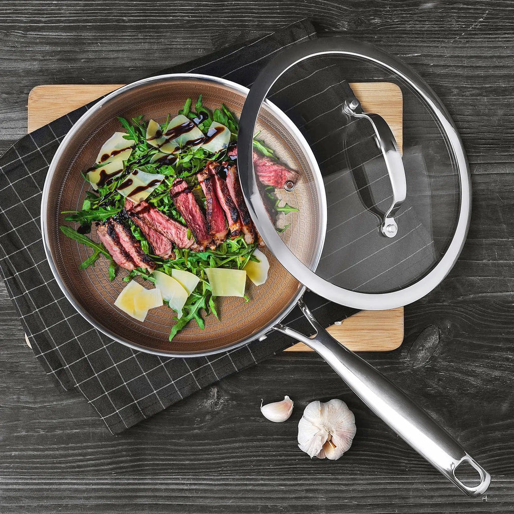 Overhead view of a frying pan with gold interior and  glass lid set aside to show cooked beef strips, rocket leaves and dressing