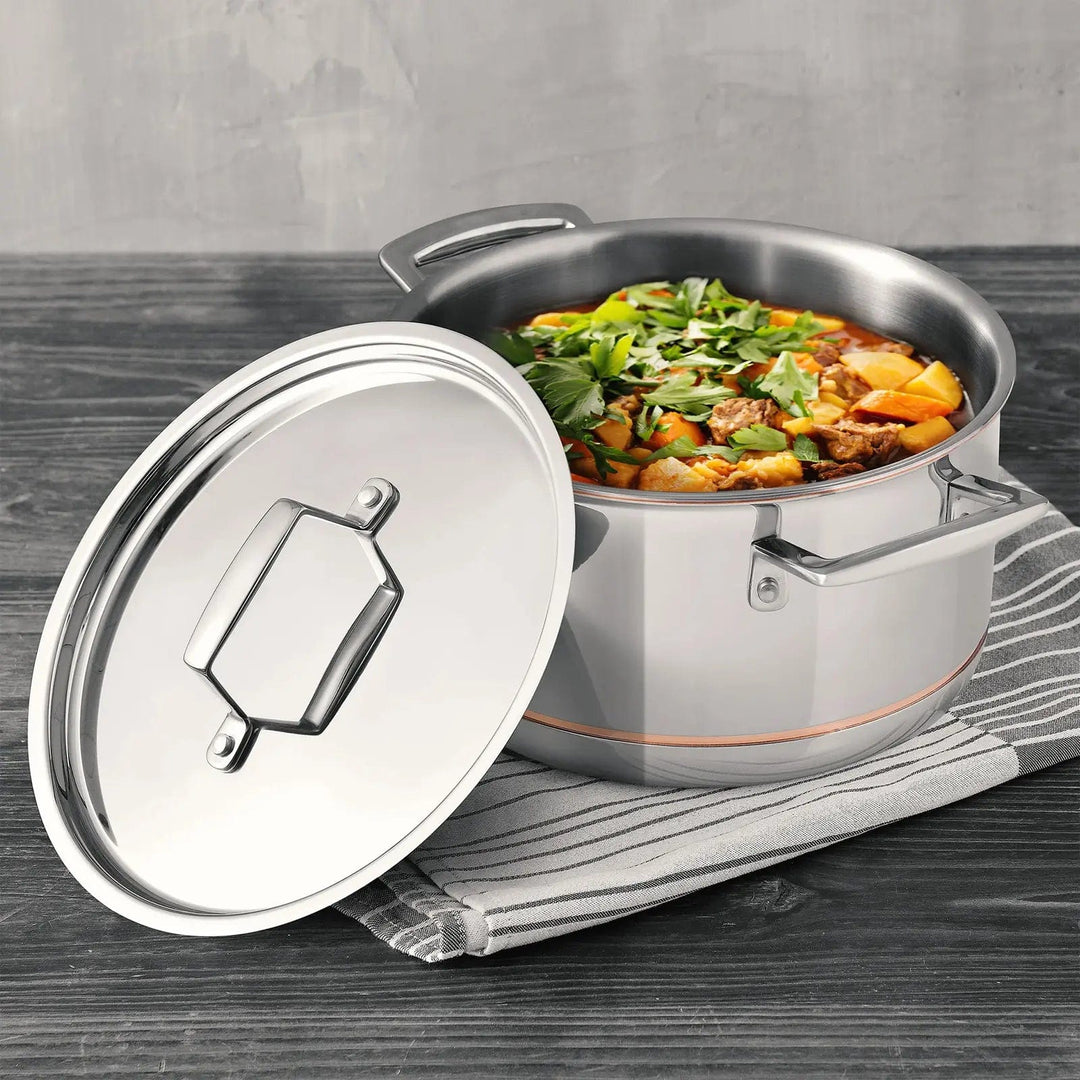 Stainless steel casserole dish with lid on hte side to show a cooked stew with vegetables and parsley, on a grey table and tea towel