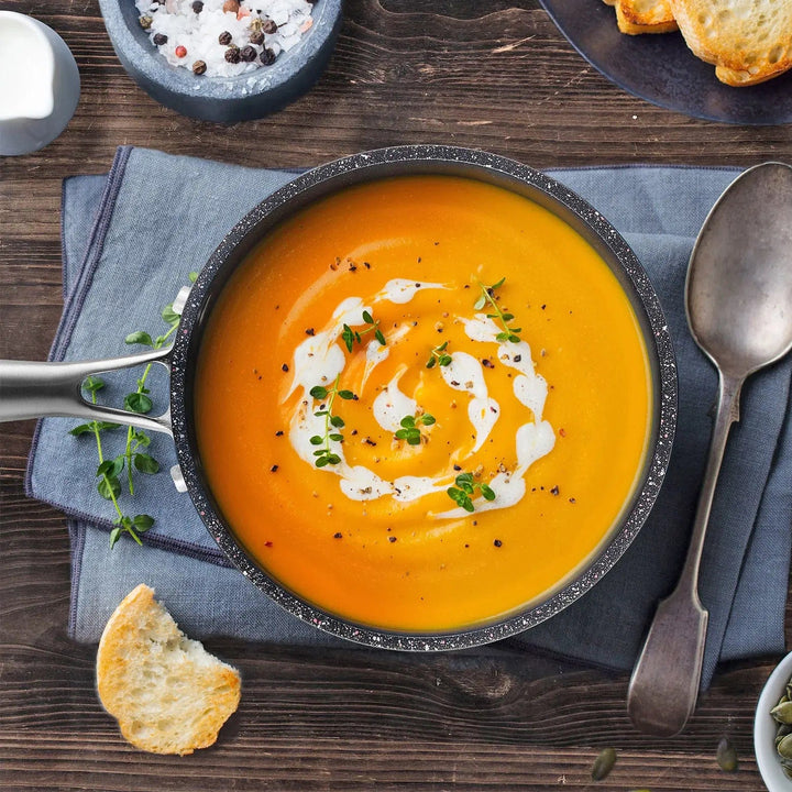 Overhead view of a small pot filled with cream of tomato soup, on a table with bread and cutlery