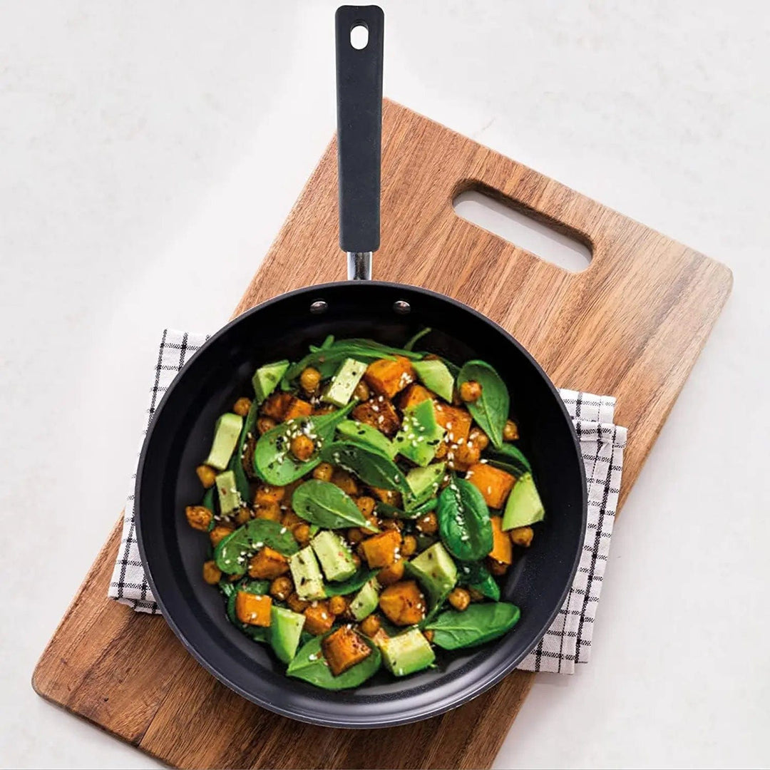 Overhead view of a frying pan with stir fry food, served on a wooden board with tea towel