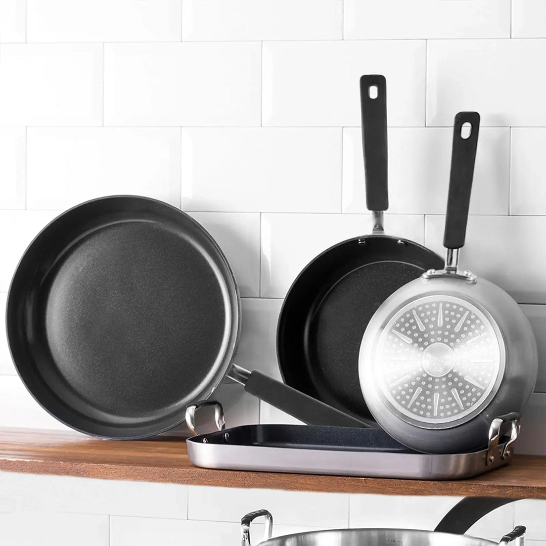 3 assorted size frying pans on a kitchen shelf with white tiled wall