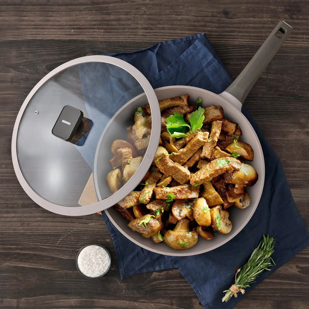 Overhead view of a brown frying pan with glass lid open to show cooked beef and mushrooms